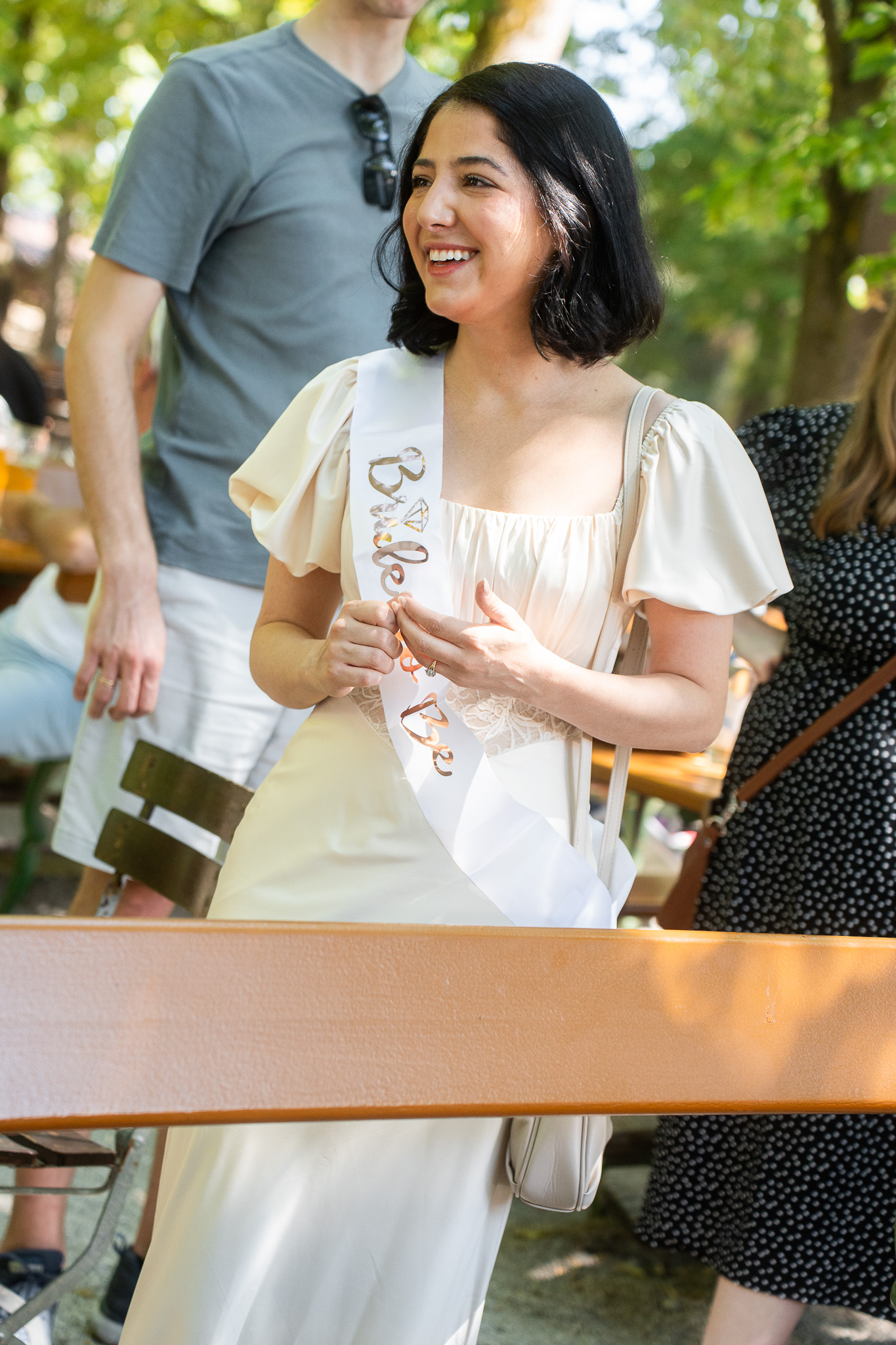 Kaitlyn lächelt mit einer Bride-to-Be-Schärpe im Spezi-Keller.